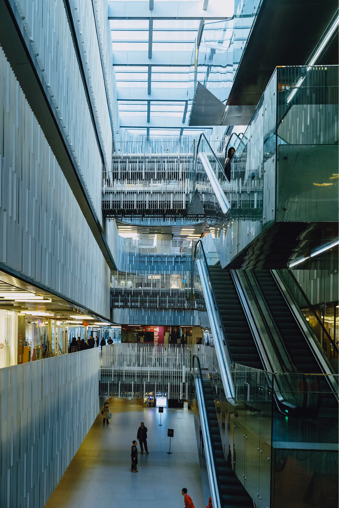 Lichthof eines Bürogebäudes mit Rolltreppen und Menschen auf den Galerien